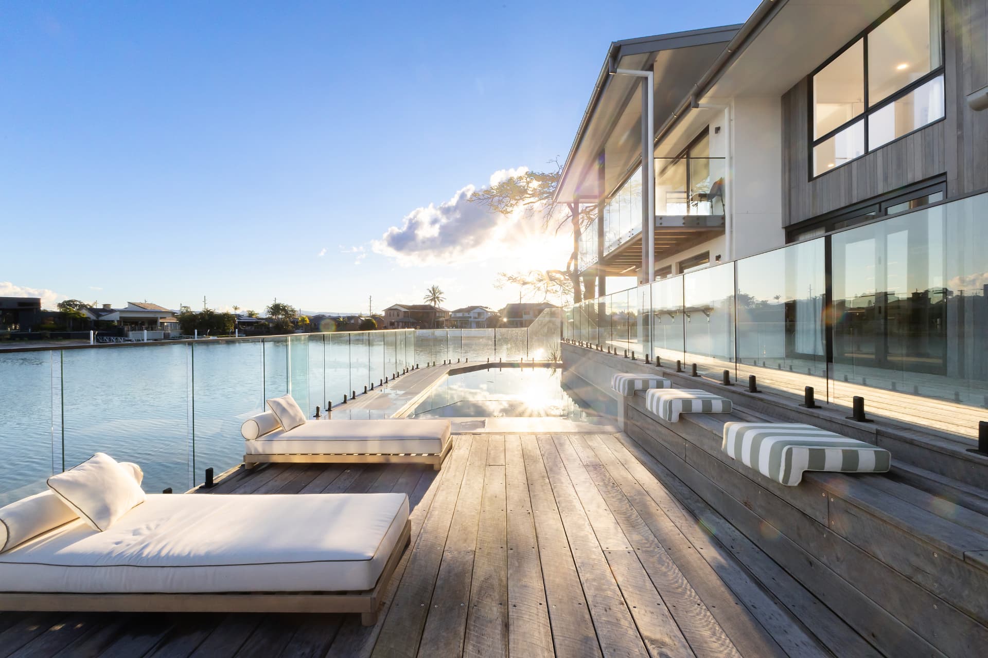 Day beds on the hardwood deck beside the pool, late afternoon sun down the canal